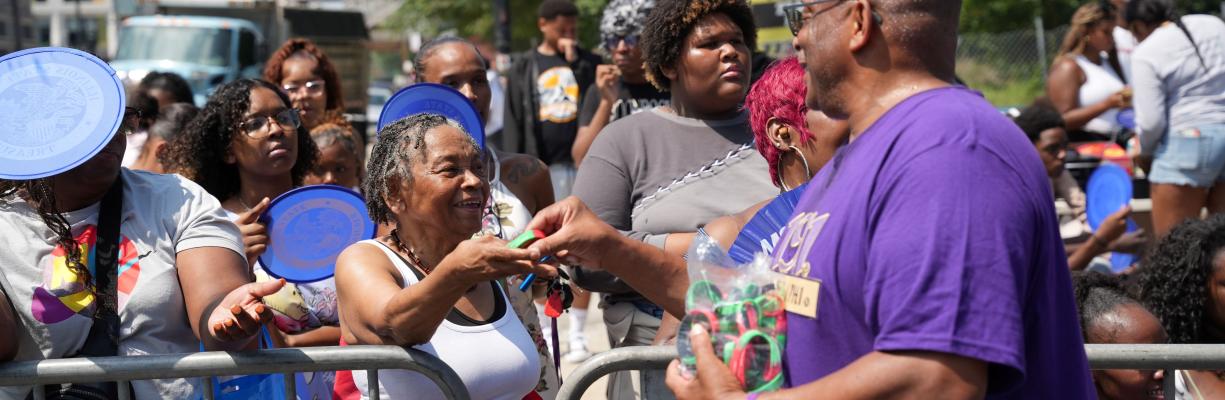 A man in a a purple shirt hands a Know Your Rights wristband to a woman during the Bud Billiken Parade.