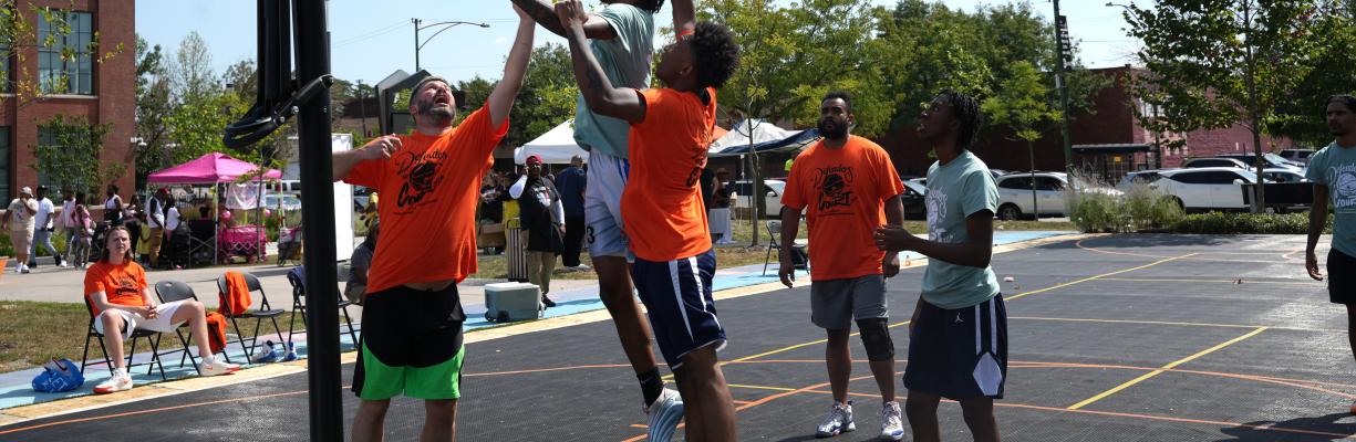 Men playing three on three basketball on a sunny day.